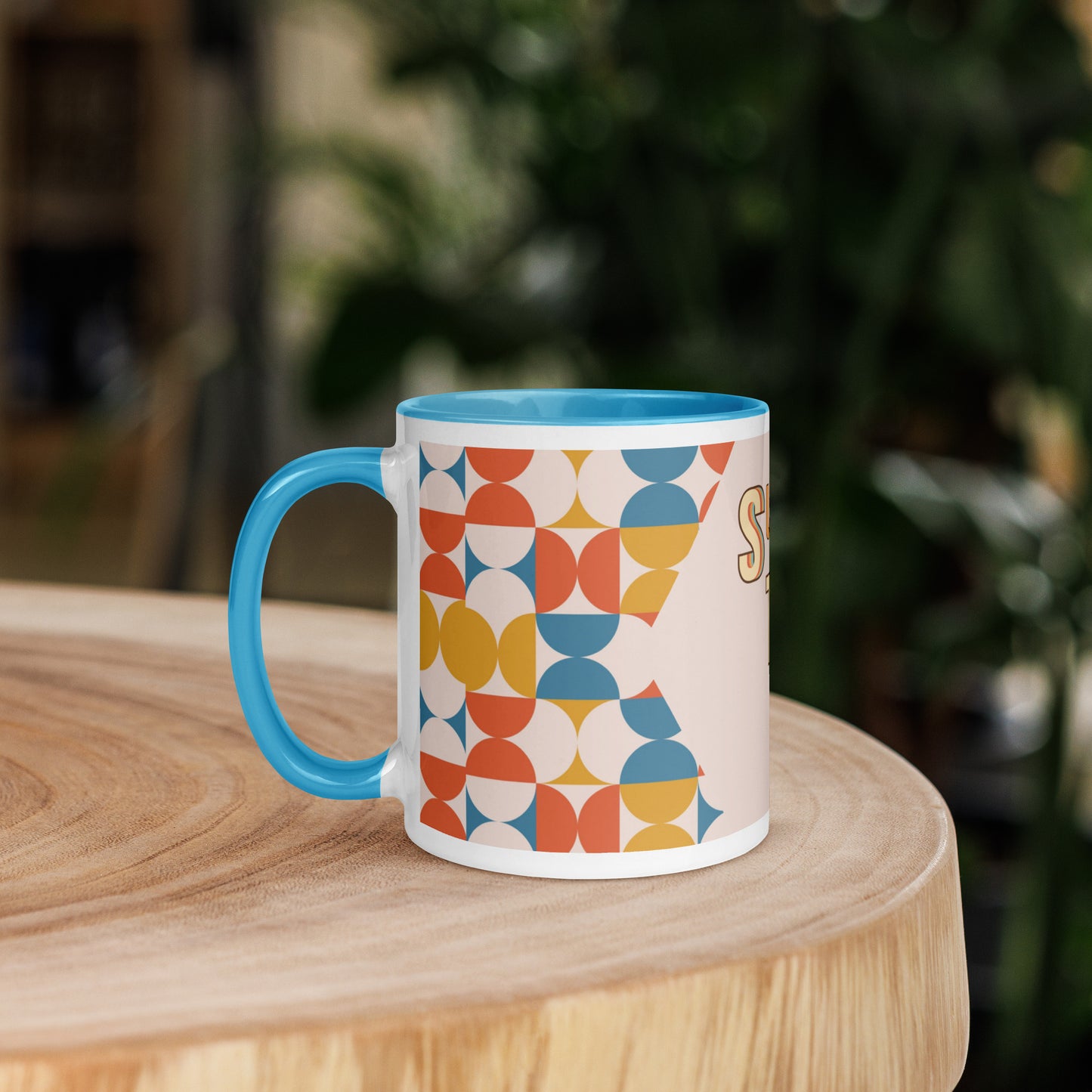 A yellow ceramic mug, named the "Slay the Day Mug," with "Slay The Day" inscribed on it and adorned with a geometric pattern, rests on a wooden table. It is both dishwasher and microwave safe for ultimate convenience.