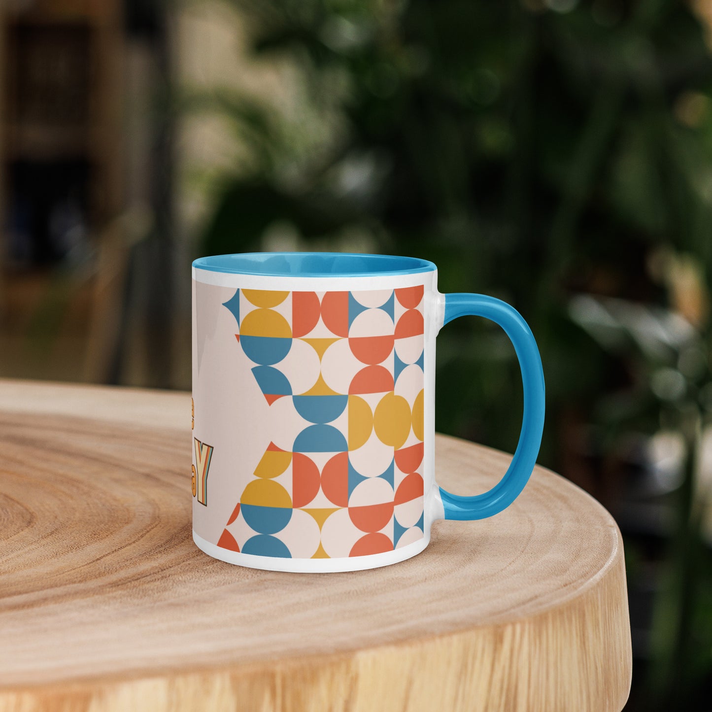 A yellow ceramic mug, named the "Slay the Day Mug," with "Slay The Day" inscribed on it and adorned with a geometric pattern, rests on a wooden table. It is both dishwasher and microwave safe for ultimate convenience.