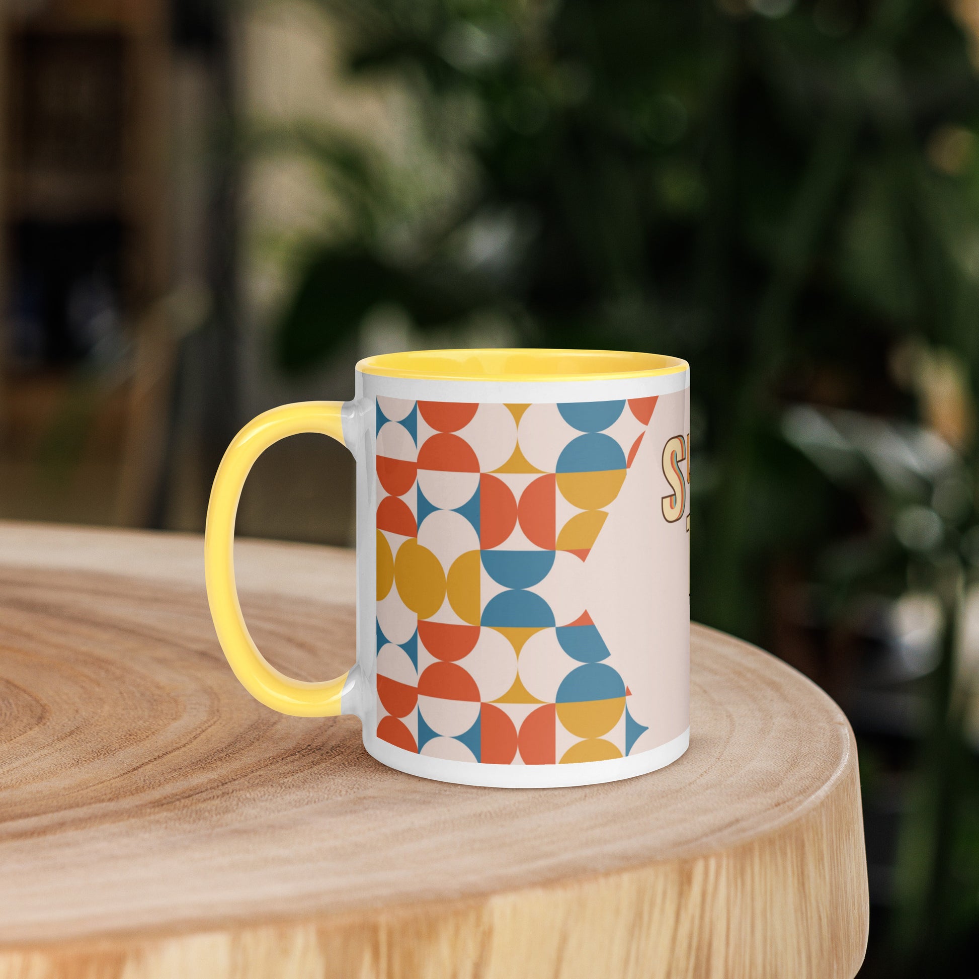 A yellow ceramic mug, named the "Slay the Day Mug," with "Slay The Day" inscribed on it and adorned with a geometric pattern, rests on a wooden table. It is both dishwasher and microwave safe for ultimate convenience.