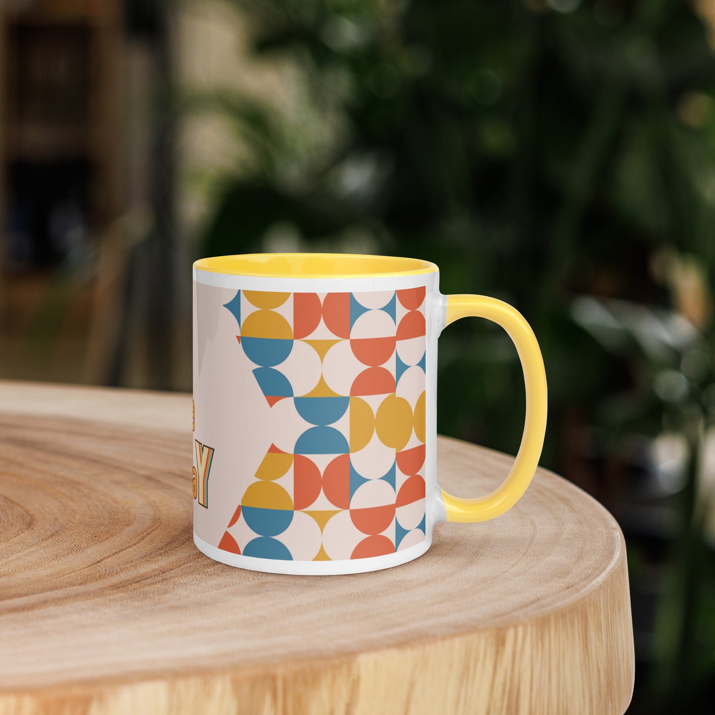 A yellow ceramic mug, named the "Slay the Day Mug," with "Slay The Day" inscribed on it and adorned with a geometric pattern, rests on a wooden table. It is both dishwasher and microwave safe for ultimate convenience.